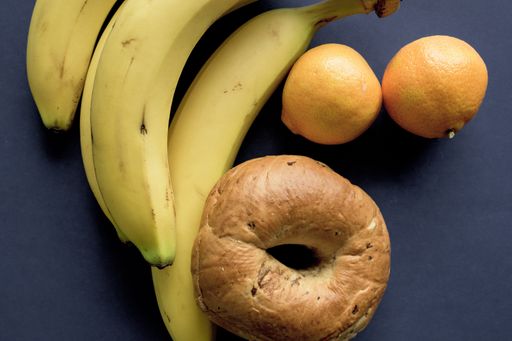 A closeup shot of a doughnut, banana, and oranges on a dark blue surface