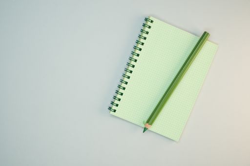 A top view of the green notepad and the green pencil on the gray surface