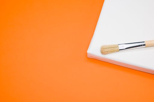 A closeup shot of the paintbrush and the canvas on the orange surface