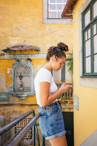 A shallow focus shot of a young beautiful Hispanic wearing a protective mask while using her mobile phone outdoors