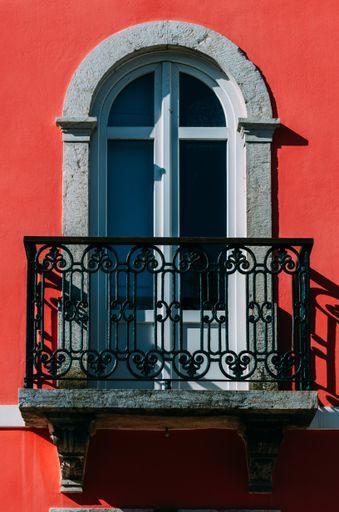 A vertical shot of an arch-shaped window with a small balcony on a building with red facade