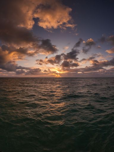 A vertical shot of a calm wavy sea under a cloudy sky during a sunset