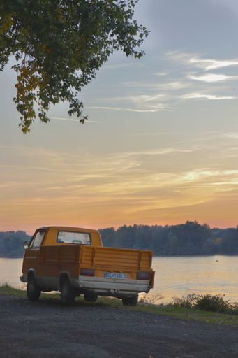 A bright yellow pick up truck is parked on the side of a road, adjacent to a tranquil body of water