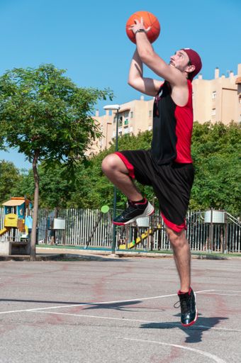A vertical shot of a young man throwing ball into the basketball basket