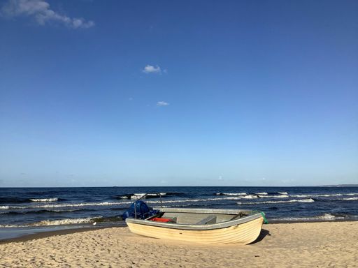 A view of single wooden fishing boat mooring by the clean sandy beach on a clear blue sky