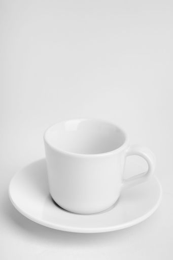 A vertical shot of a white cup of coffee with its plate on a white surface