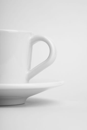 A vertical shot of a white cup of coffee with its plate on a white surface