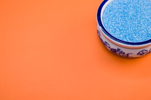 A high angle shot of blue sand in a china bowl on an orange surface