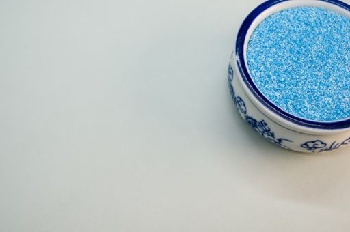 A high angle shot of blue sand in a china bowl on a white surface