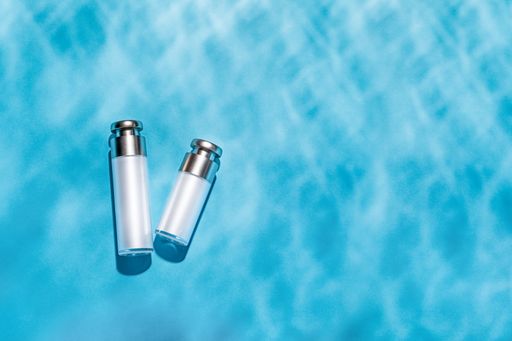 A top view of skincare bottles on a bright blue water surface