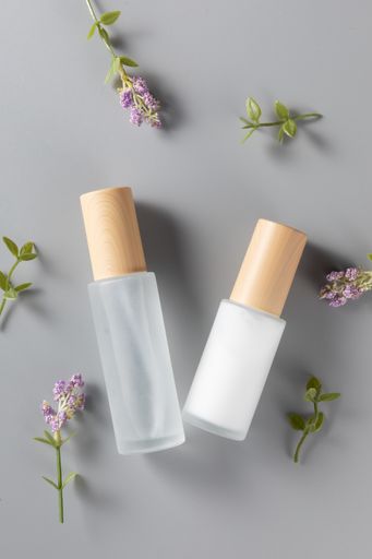A vertical top view of skincare bottles on a surface with lavender flowers
