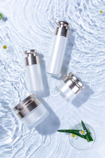A vertical top view of skincare bottles on a white water surface