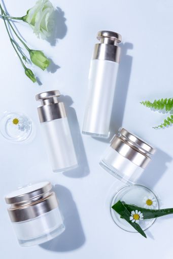 A vertical top view of skincare bottles and containers on a white surface with flowers