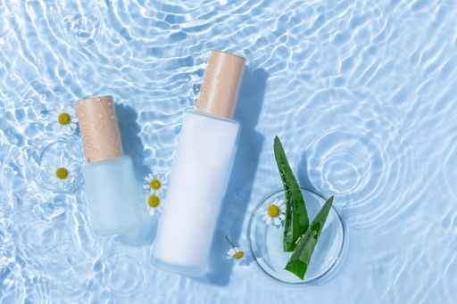 A top view of skincare bottles on a light blue water surface with aloe vera and daisy flowers