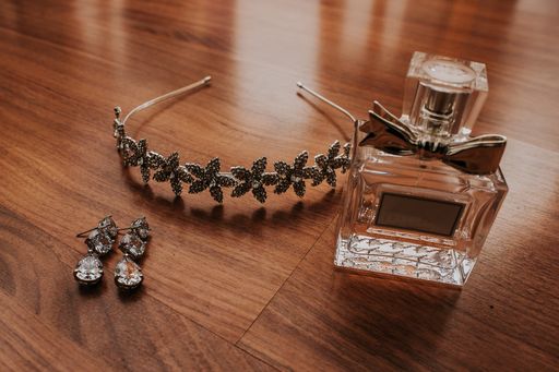 A closeup shot of  a headband, perfume, and a pair of earrings on a smooth wooden smooth surface