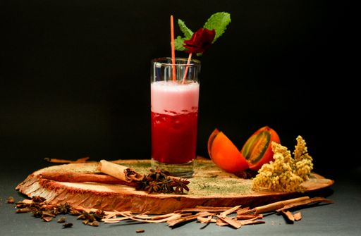 A glass of fresh beverage on a wooden board with cinnamon pieces, star anise, and naranjilla fruit