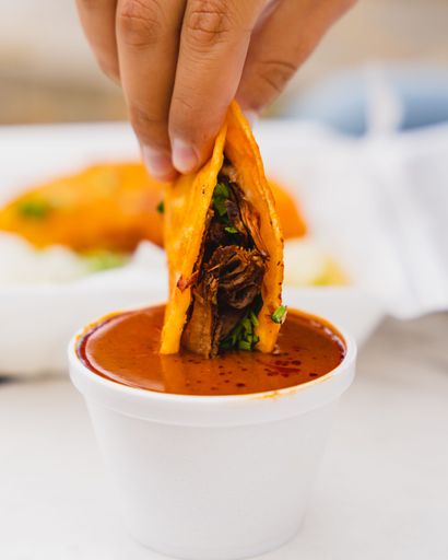 A vertical closeup of a birria taco being dipped into consome