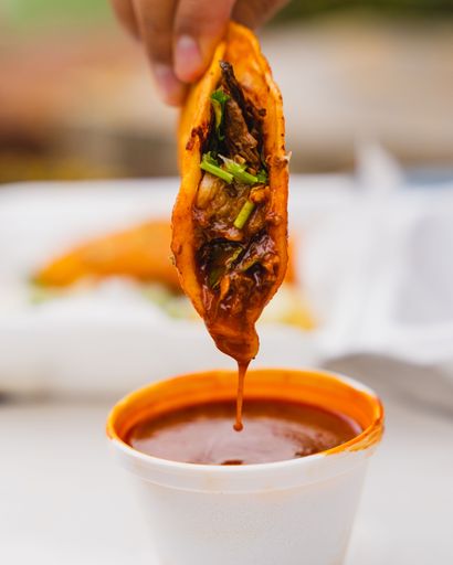 A vertical closeup of a birria taco being dipped into consome