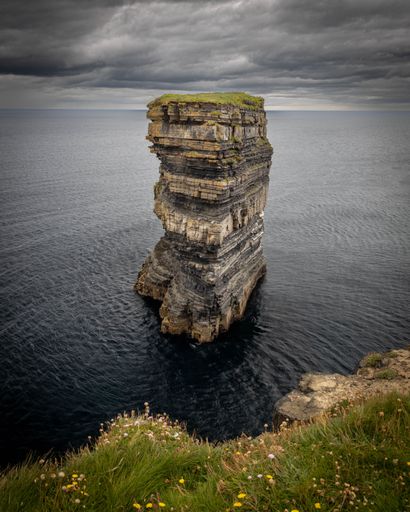 A vertical drone shot of the Downpatrick Head on the coast under the gloomy sky in Ireland