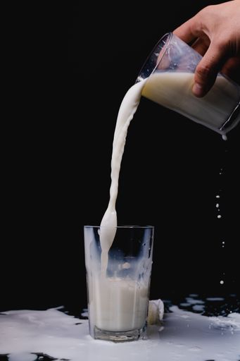 A closeup shot of milk being poured in a glass cup on a black background