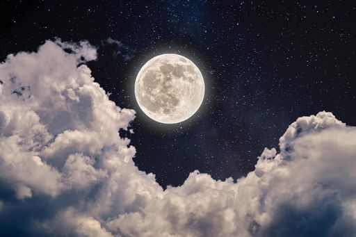 A beautiful shot of the full moon in the night sky full of stars and cumulus clouds
