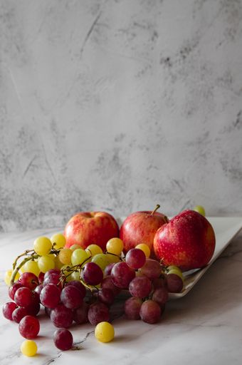 A closeup of red apples and grapes on a plate isolated on a marble surface
