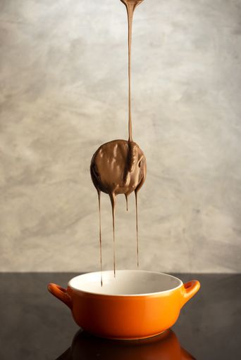 A vertical shot of a piece of cake floating in the air with melted chocolate pouring over it