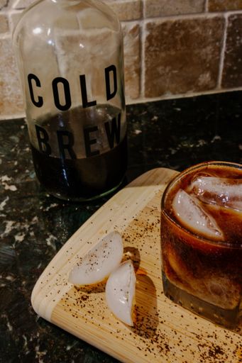 Cold brew coffee concept with a glass of iced cold brew coffee, a cold brew glass storage bottle, and scattered ice cubes and coffee grounds