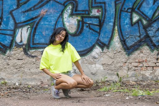 A female in a bright yellow t-shirt and blue shorts against the background of a wall with graffiti