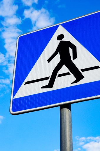 A vertical shot of a traffic sign showing crossing pedestrian