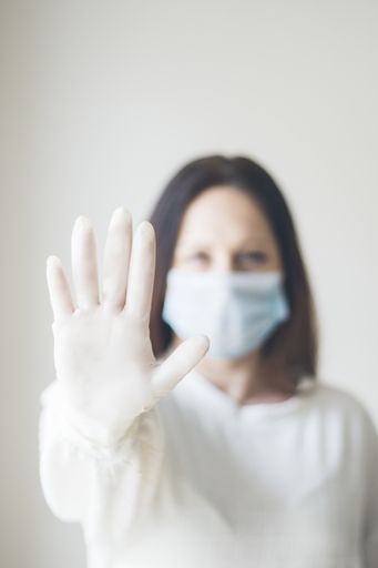 A vertical shot of a young woman wearing a sanitary mask showing a "stop" sign with her hand