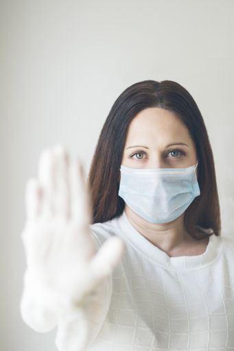 A vertical shot of a young woman wearing a sanitary mask showing a "stop" sign with her hand