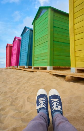 A vertical shot of a person lying on the sand near the colorful huts