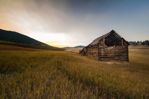 A majestic shot of an old wooden barn on a hillside of a grassy farm
