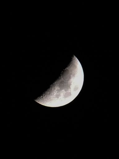 A vertical shot of the half moon in the dark night sky
