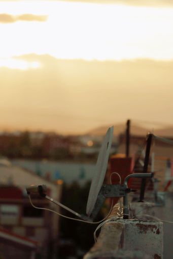 A selective vertical shot of a small dish antenna attached to the edge of a roof wall at the sunset in Valencia, Spain.
