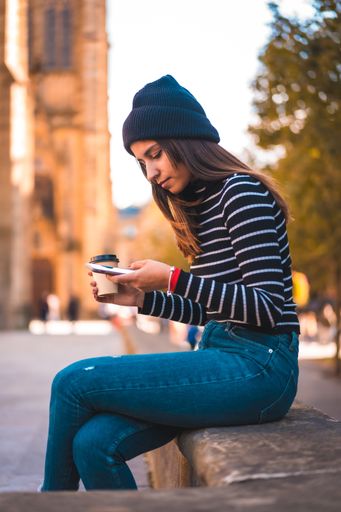 A vertical shot of a female using her phone while drinking coffee