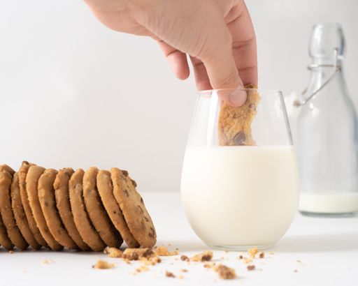 A soft focus of a person dipping a chocolate chip cookie into a glass of milk