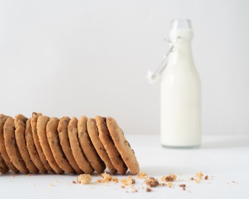 A soft focus of a bitten chocolate chip cookies and crumbs with blurry milk bottle in the background
