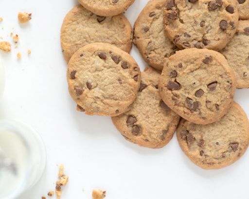An overhead shot of chocolate chip cookies and crumbs on white surface