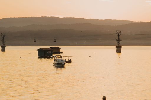 A pinkish view of a lake, houseboats,cable cars over the waters during the sunset and the silhouette of mountains on the horizon
