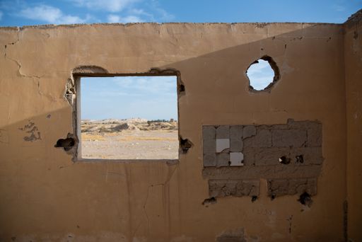 Old building ruins seen through a cracked wall made of concrete with an opening in the Negev desert