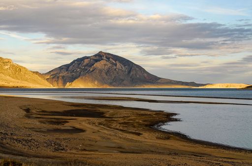 A scenic shot of the bank of a river with a rocky hill on the background
