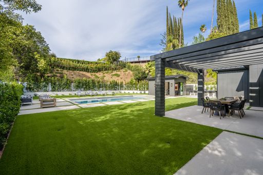This image shows an outdoor patio overlooking a stunning swimming pool, with a modern living room in the background