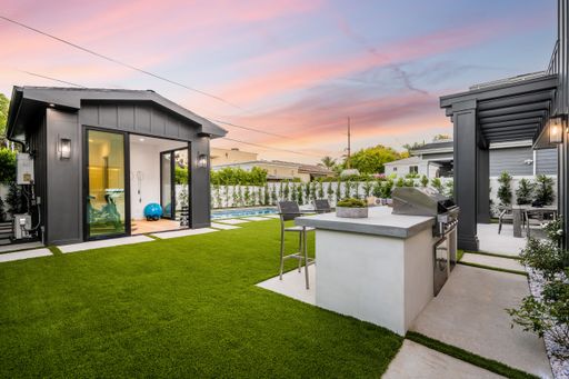 A contemporary outdoor living area featuring a large lawn and a stainless steel gas grill, ideal for hosting summer barbecues