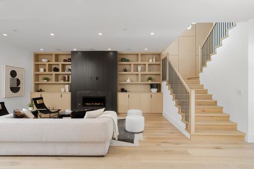 A contemporary living room features cozy beige furniture, gleaming hardwood floors, and a stunning open fireplace