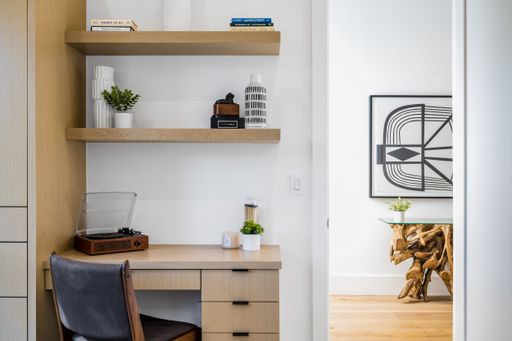 A contemporary looking wooden office desk with storage shelves on the wall behind it, offering a functional and stylish workspace