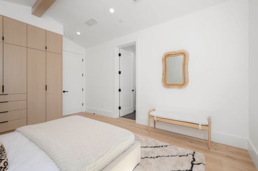 A modern bedroom interior featuring a white bed with white bedding atop a hardwood floor