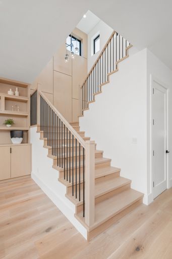 A wooden staircase featuring a white balustrade, illuminated with natural light from a nearby window, leading to the upper level