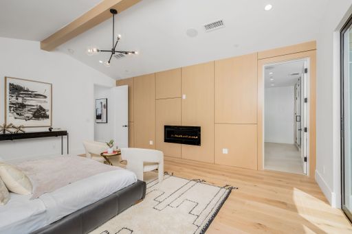 A modern bedroom with white and wood accents and a vaulted ceiling featuring recessed lighting